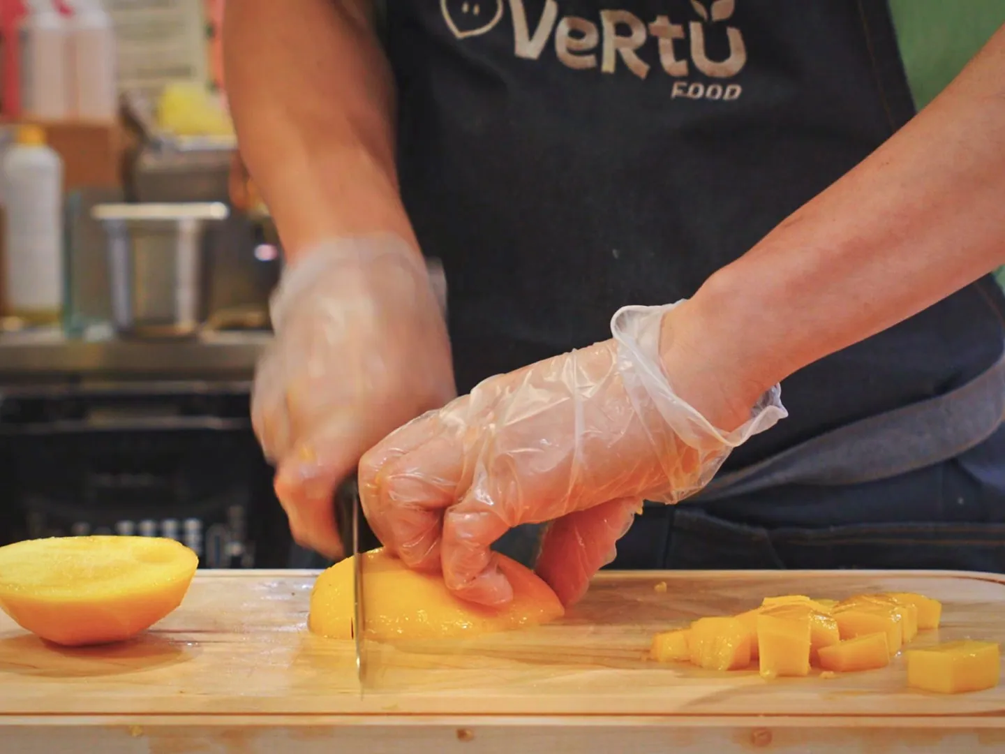 Mangue taillée en cubes par une préparatrice au tablier Vertu Food