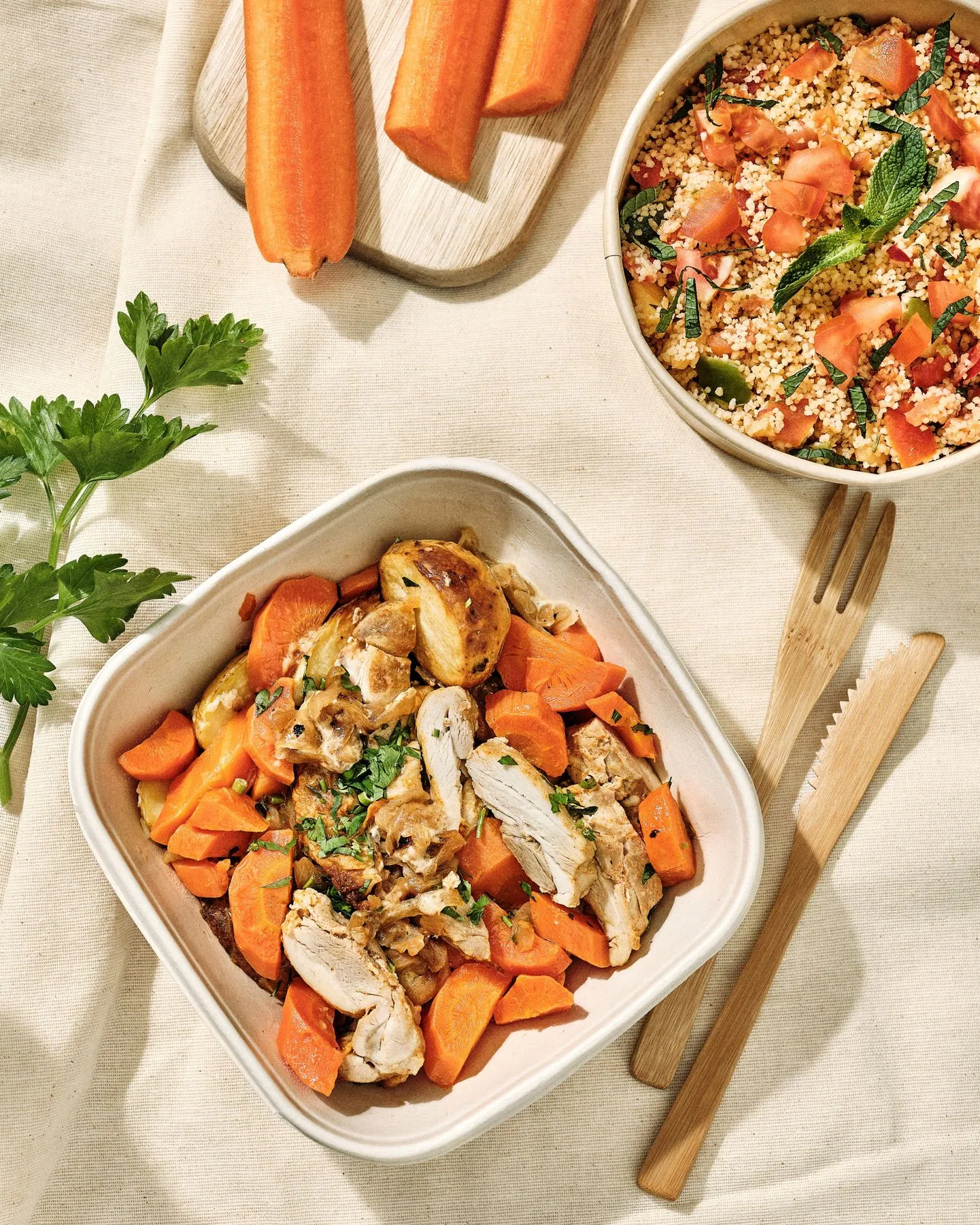 Poulet aux carottes et taboulé dans des barquettes, sur une nappe en lin